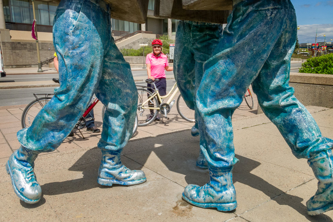 A cyclists in pink stares out between a giant sculpture depicting two pairs of legs engaged in a fight Picture