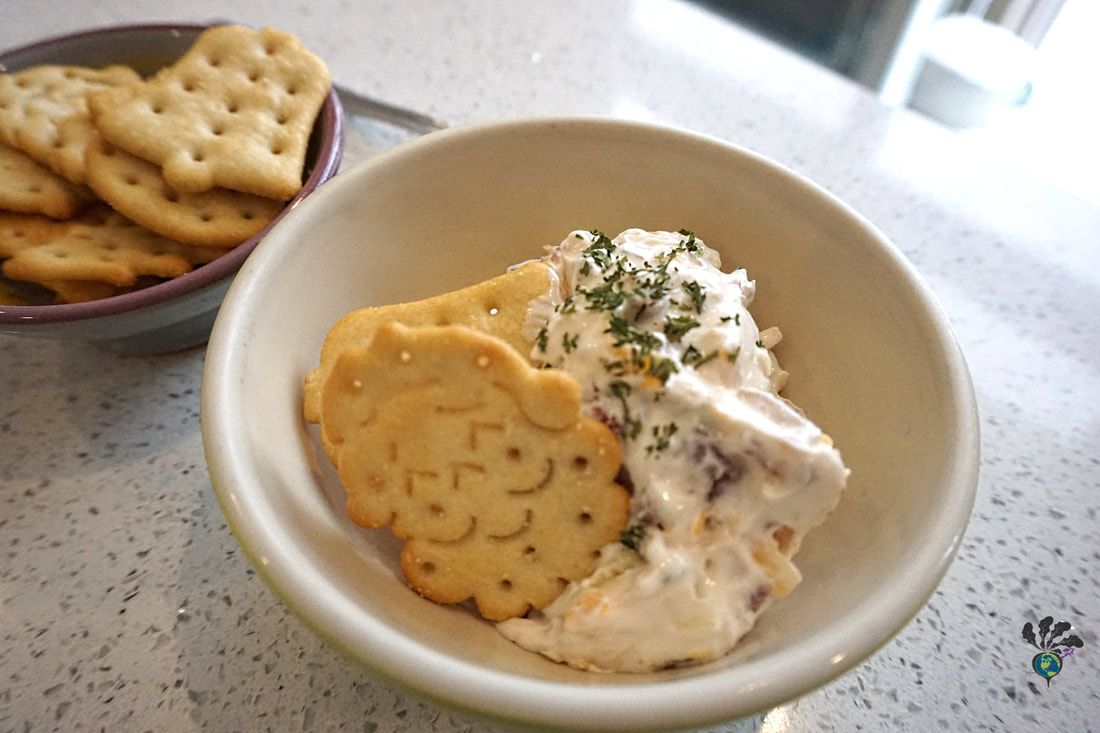 A scoop of loaded baked potato chip dip sits in small white bowl with crackers on the side 