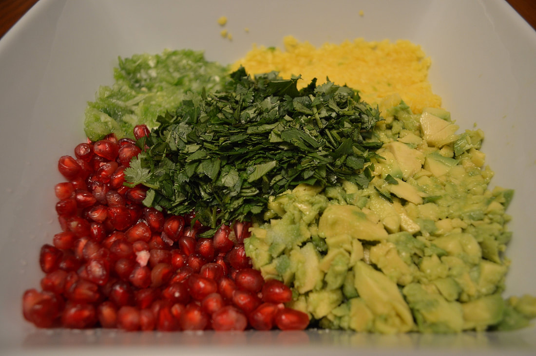 Avocado, pomegranate seeds, cilantro, and more chopped ingredients sit in a white bowl Picture