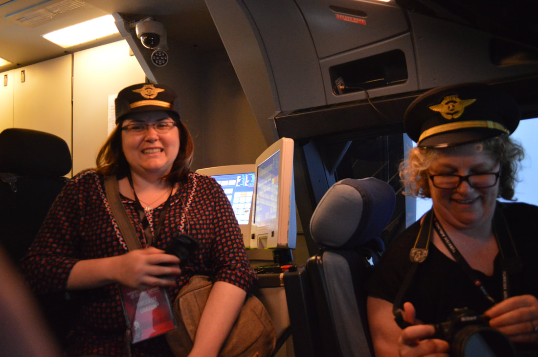 Vanessa and a friend wear pilot caps and sit in a flight simulator 