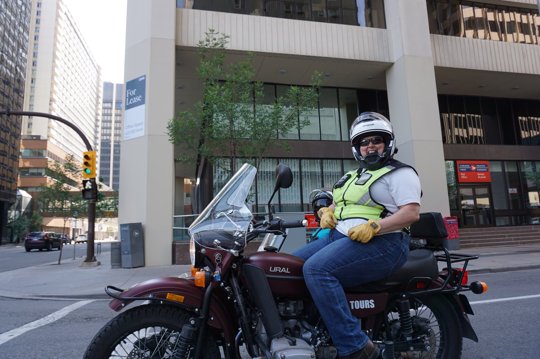 A woman rides a burgundy Ural motorcycle while wearing a yellow reflective vest.Picture
