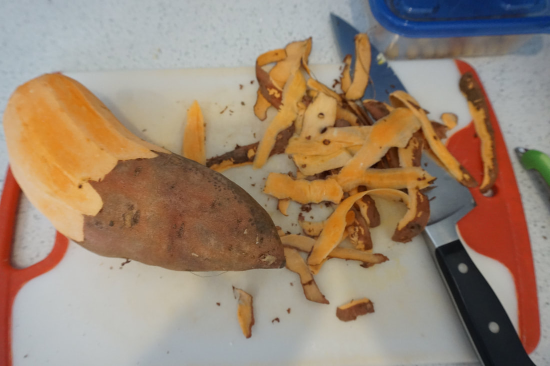 A large sweet potato sits partially peeled on a cutting board