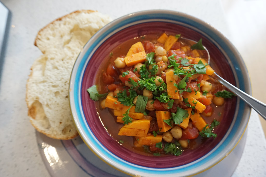 Overhead shot of the blue and purple bowl filled with chickpea and sweet potato stew, with bread on the side