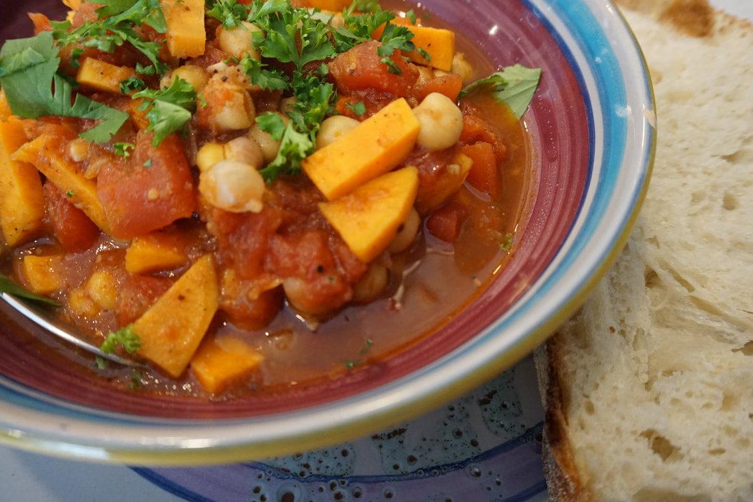 Colourful bowl of chickpea and sweet potato stew with a slice of bread on the side.