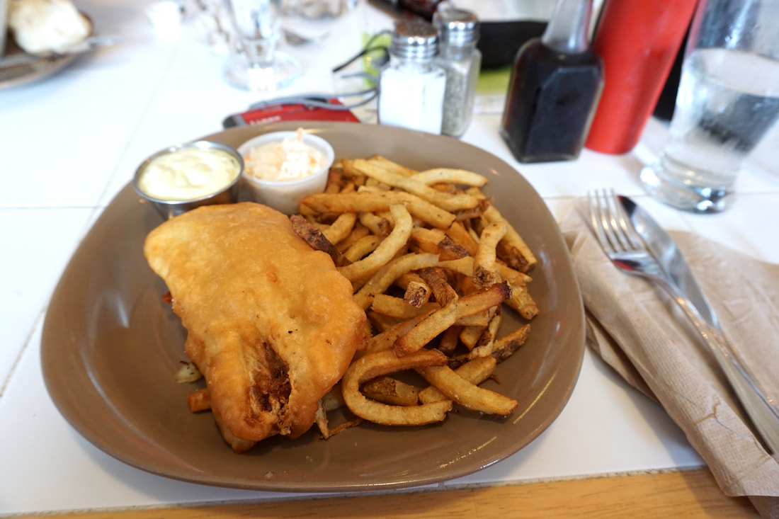 A brown plate holds fish and chips, with restaurant condiments in the background.