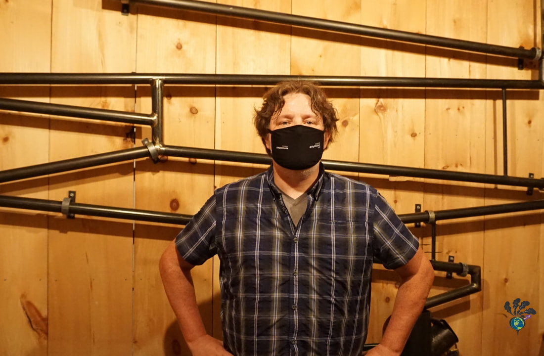 Ryan poses in a blue shirt against a wooden wall with pipes on it at Escape Manor 