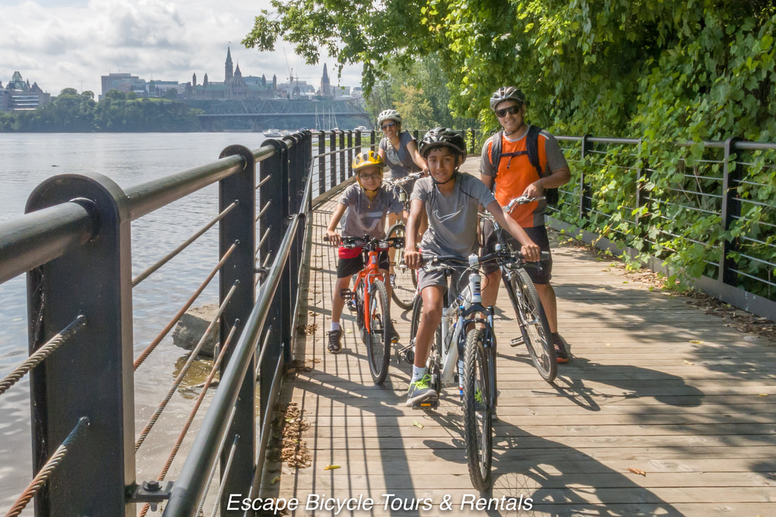 A family poses with their bikes on a waterfront bike path with the Parliament buildings in the distant backgroundPicture