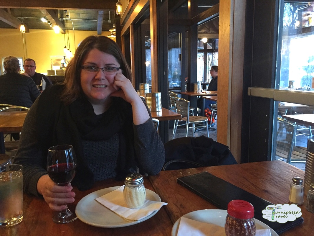 Vanessa wears a black sweater and sits in a restaurant holding a glass of red wine.