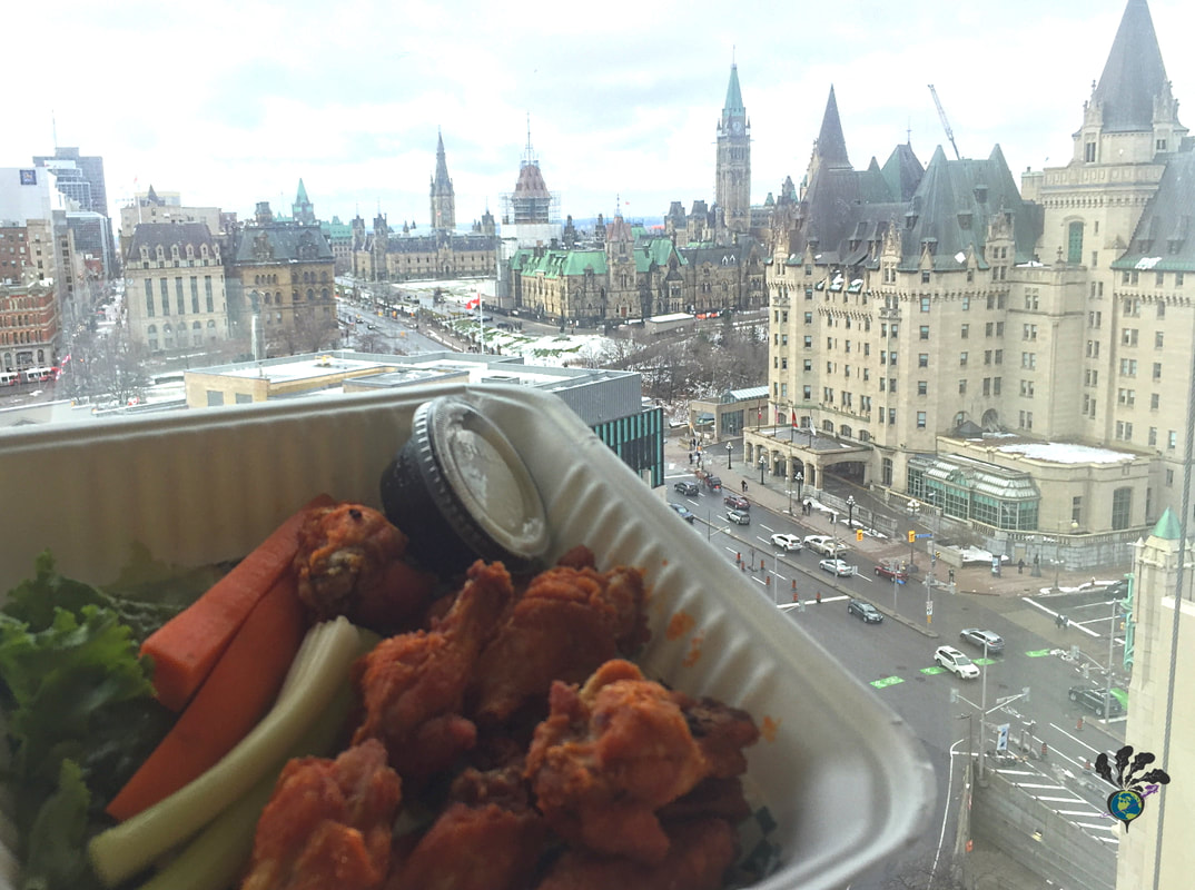 Container of chicken wings in front of a large window showing downtown Ottawa, including the Chateau Laurier hotel and the Parliament buildingsPicture