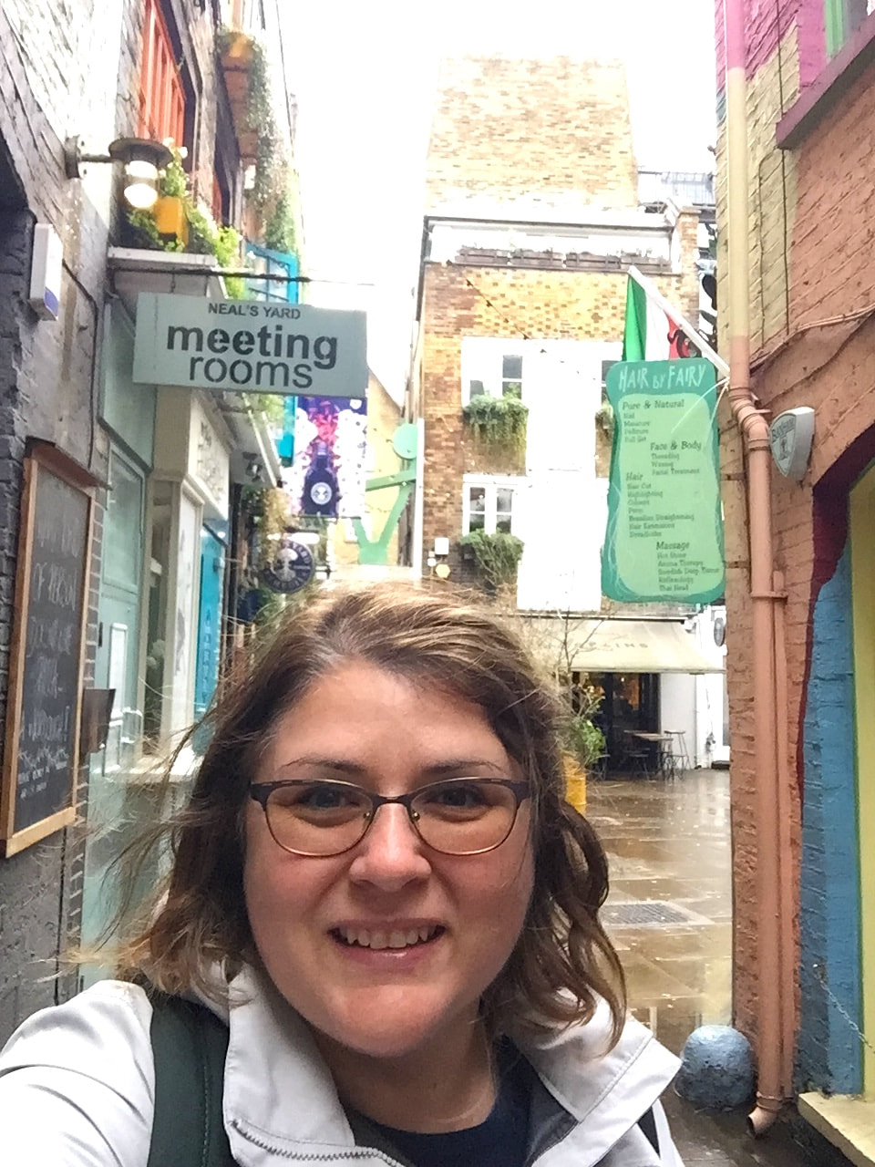 Selfie of Vanessa wearing a light grey raincoat, with the buildings of Neal's Yard in the background.Picture