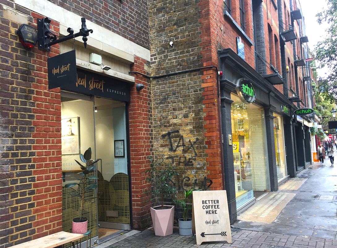 Exterior of Neal Street Espresso, a brick building with three potted plants outside, a sandwich board which says 