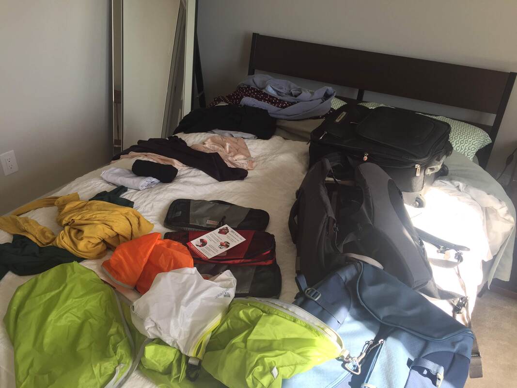 A bed covered with packing supplies like suitcases and shirts