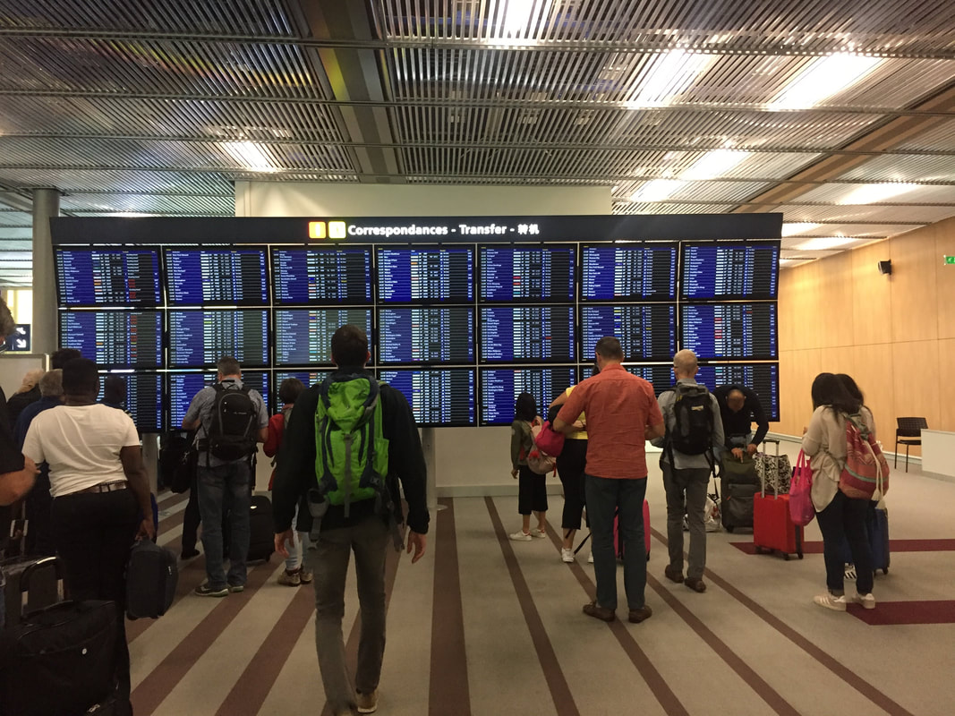 Travelers look at a giant departures board in Paris airport.