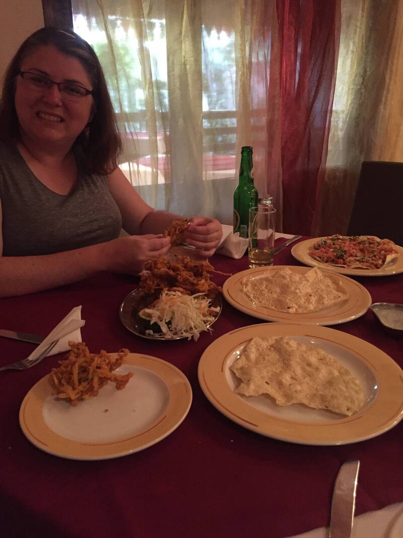 Vanessa smiles while picking up food on a table set with different Indian dishes