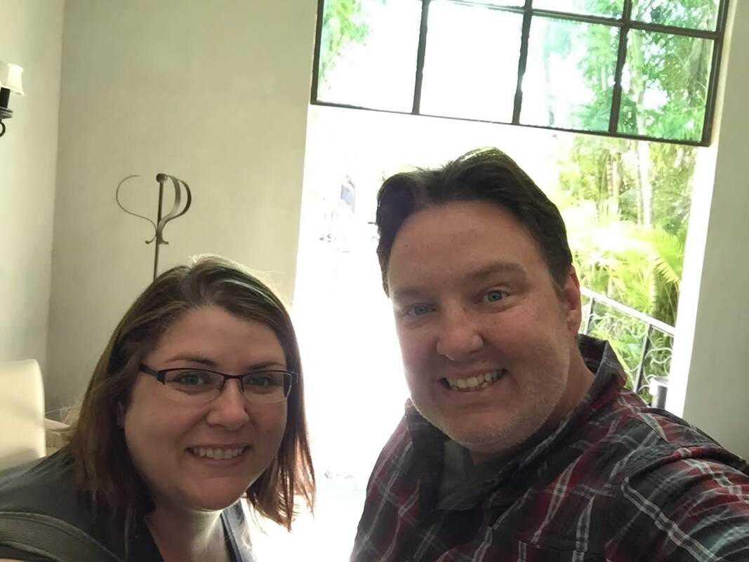 Ryan and Vanessa take a selfie in the corridor of their hotel with green plants in the background.