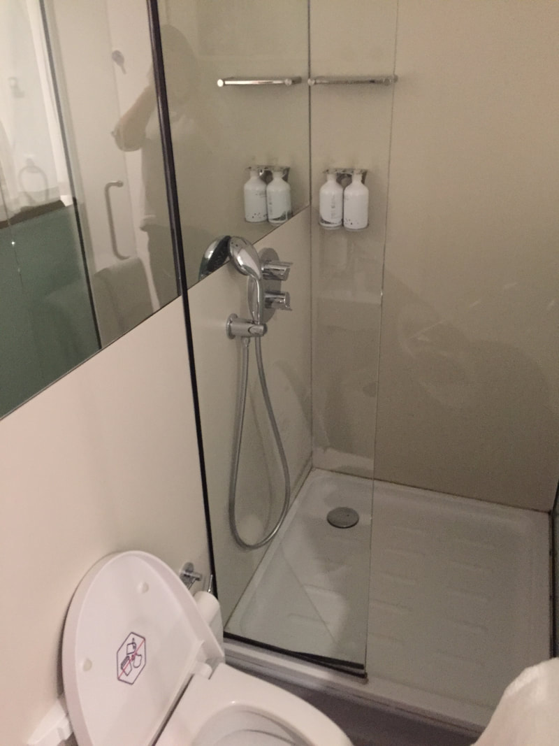 A photo of the airport sleeping pods shower room, showing a glass shower door and toilet