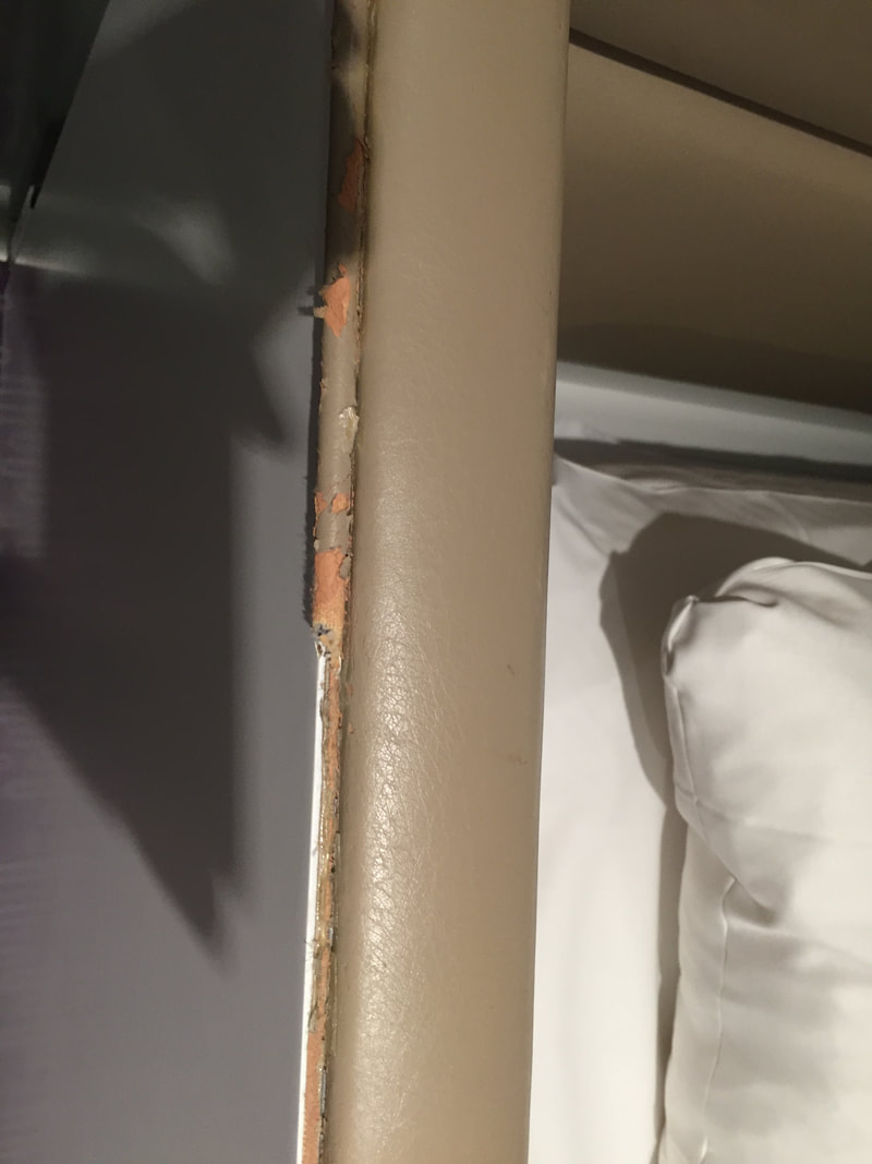 Bedframe covered in tan vinyl which is tearing and chipping