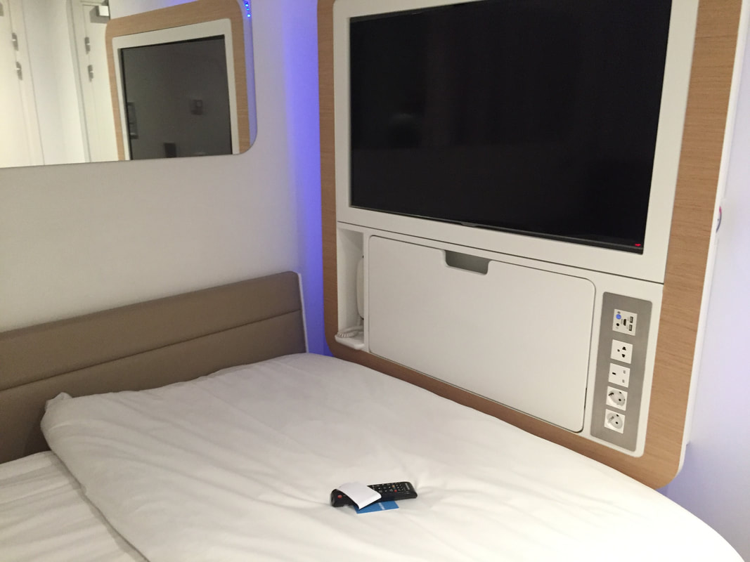 Airport sleeping pods, showing a bed, a TV and tech wall, and a mirror.