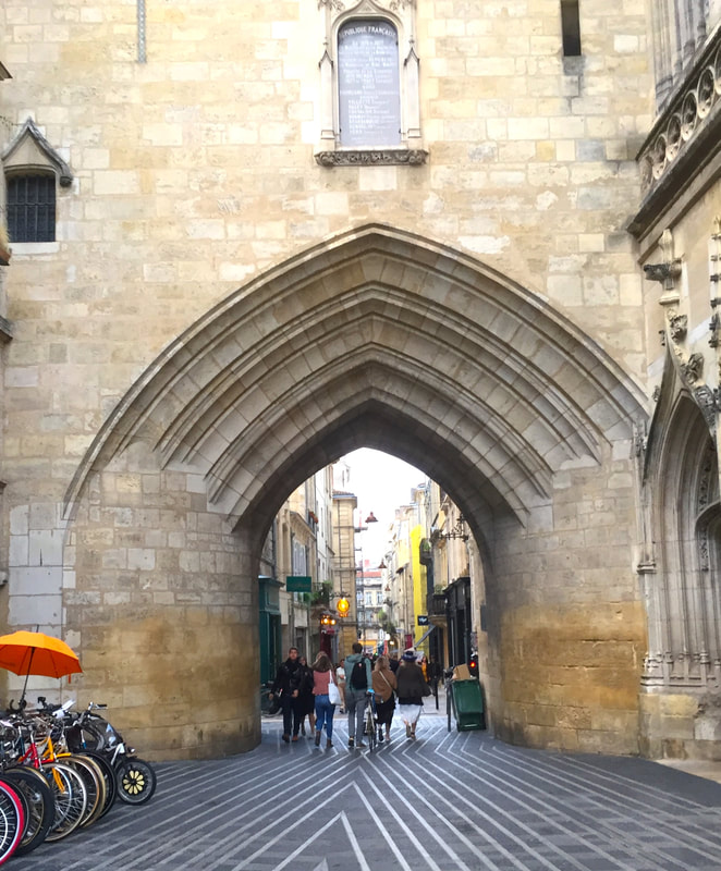 Elaborate stone archway in a building opens up to a pedestrian shopping street in the distance.