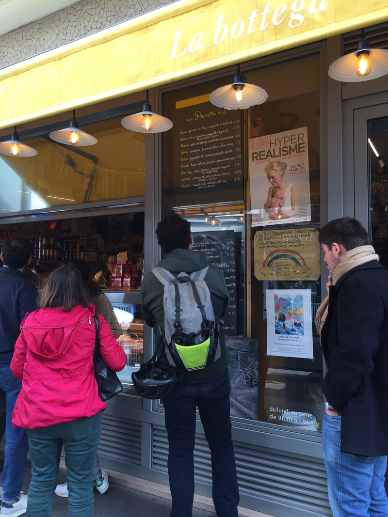 People stand in line outside a sandwich shop.