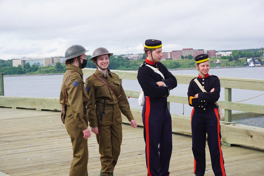 How to explore Georges Island National Historic Site, Halifax: Four costumed interpreters, two in olive grey uniforms, two in blue and red uniforms, stand on the dock.