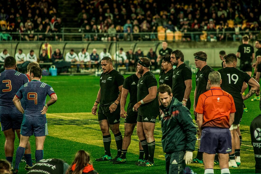 New Zealand and French rugby players stand on the field with officials and spectators in the background Picture