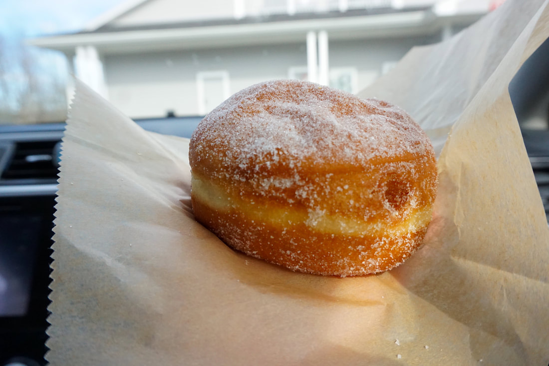 Close up of a jelly donut covered in granulated sugar, sitting on a piece of wax paper.