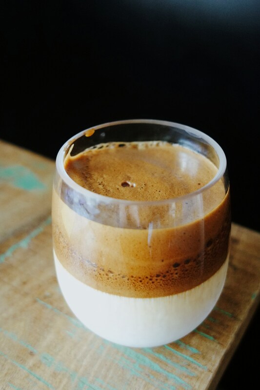 Clear glass showing a Dalgona latte with white milk on the bottom and brown coffee foam on top.Picture
