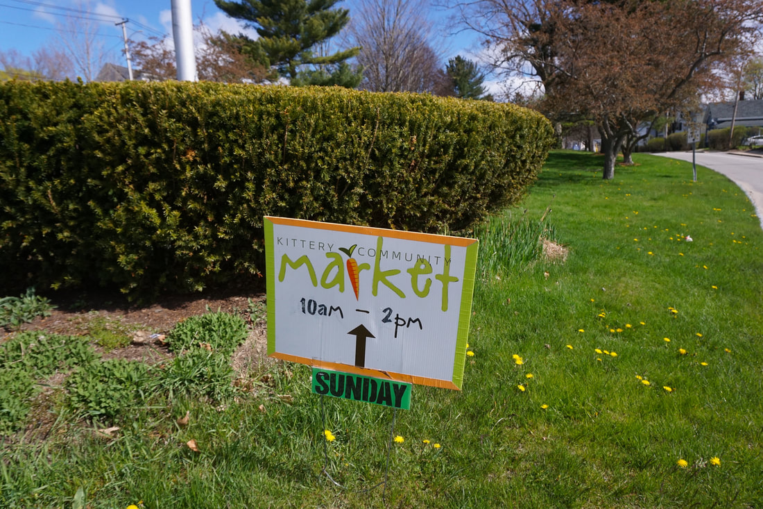 Green, white, and orange market sign placed in the ground at the edge of a public park