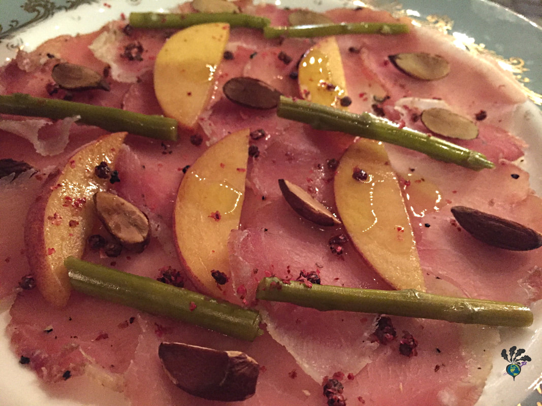 Plate of cured lonzo pork sprinkled with peach slices, almond, peppercorn, and small pieces of asparagus at North and NavyPicture