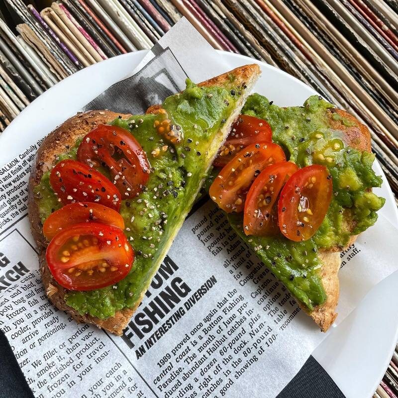 A plate showing a slice of avocado toast topped with cherry tomatoes and poppyseeds, cut in half.