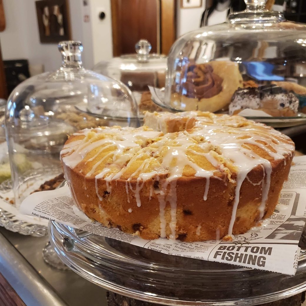 Glass cake display cafes at a cafe, one showing a large coffee cake with drizzled icing