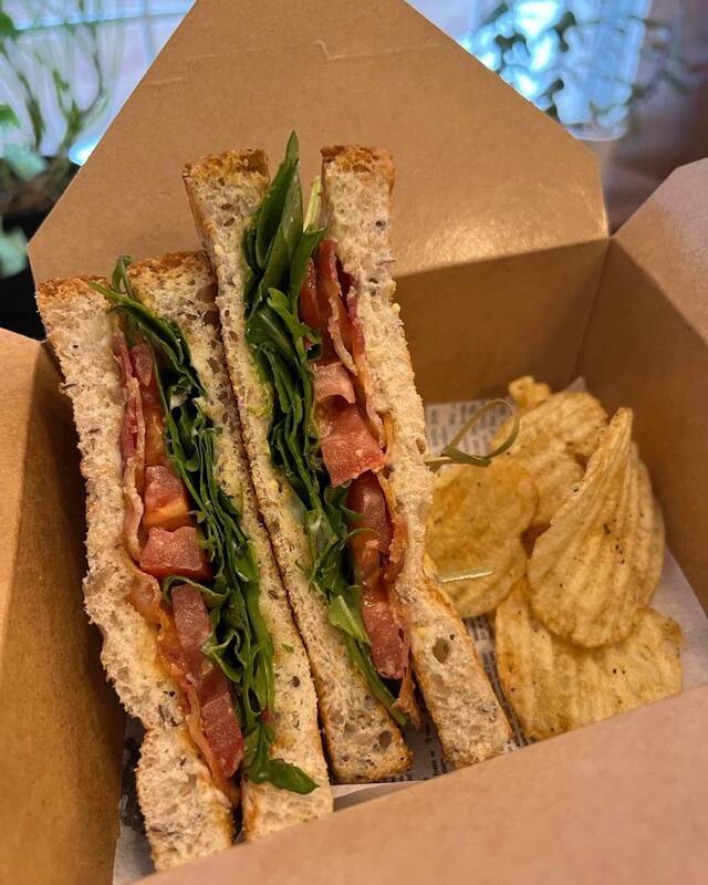 A takeout box showing a BLT sandwich on wholegrain bread with five crinkle chips on the side