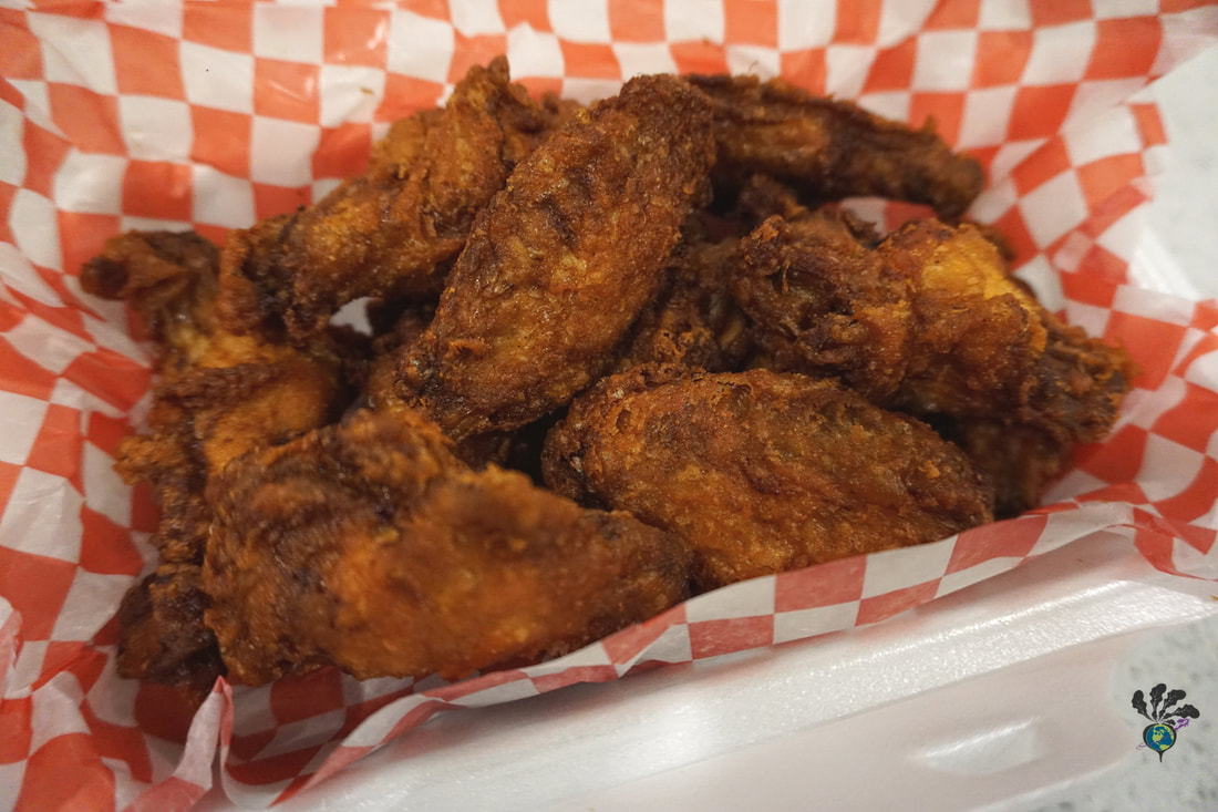 A container of crispy breaded wings sit in a takeout container lined with red and white checkered paper