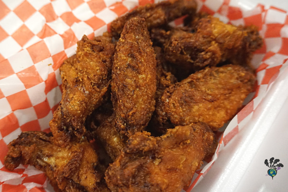 Golden brown crispy wings sit in a takeout container lined with red and white checked paper