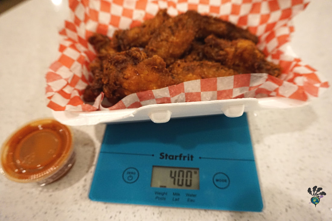 Takeout wings sit on a blue kitchen scale measuring 400 grams
