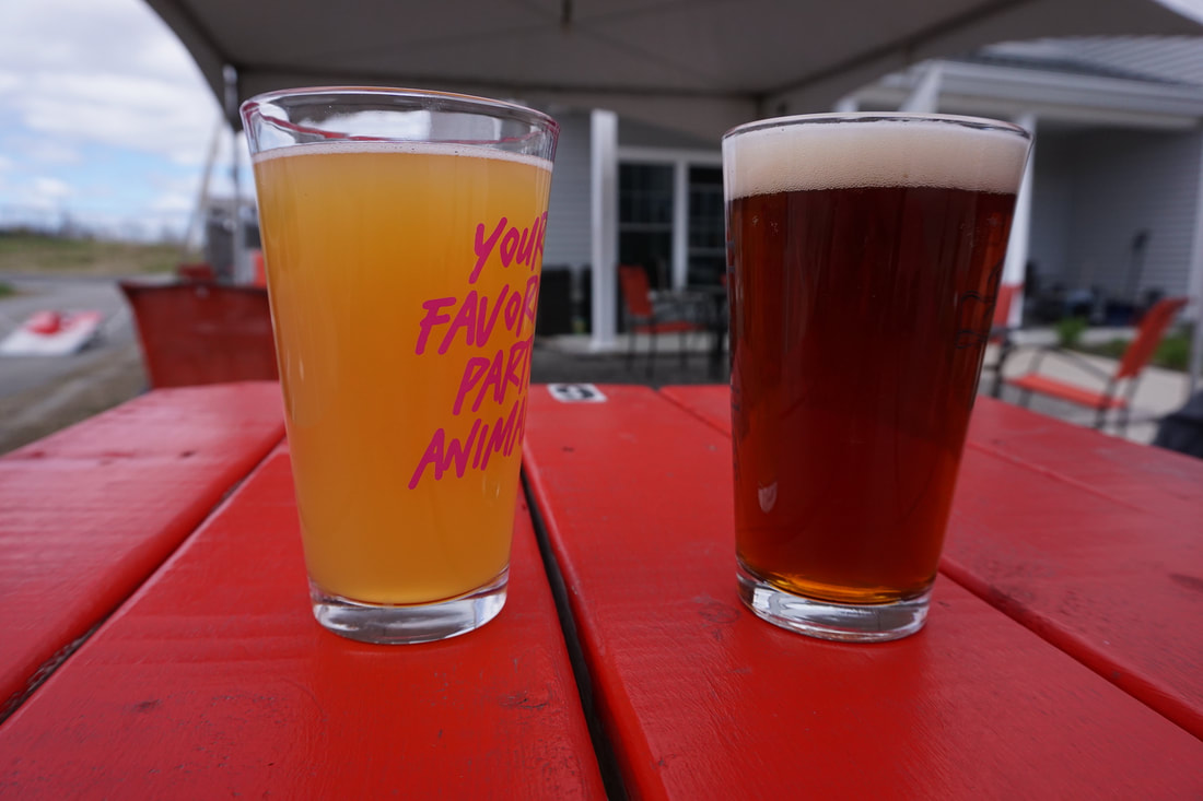 A pint of cider and a pint of red ale on a red picnic table.