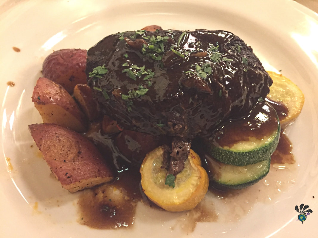 Plate of steak topped with demi glace and parsley flakes on top roasted potatoes and zucchini. Many Glacier Hotel Picture
