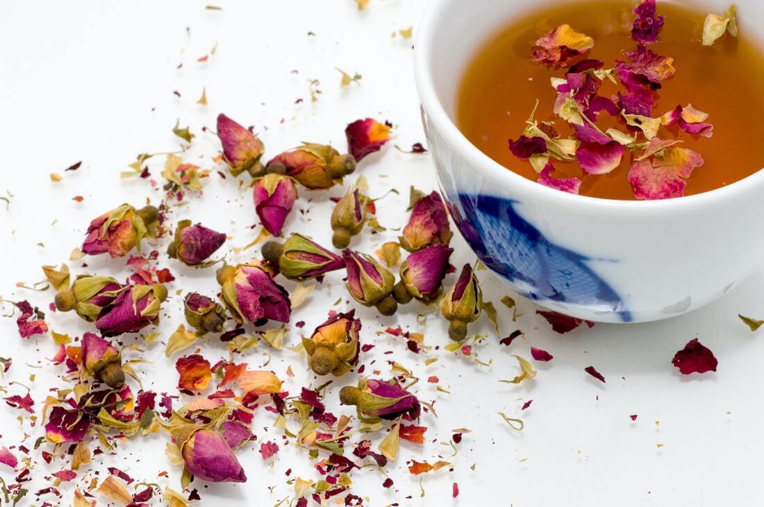 White china cup with blue designs is filled with rose petal tea, with more tea spilled on the white countertop