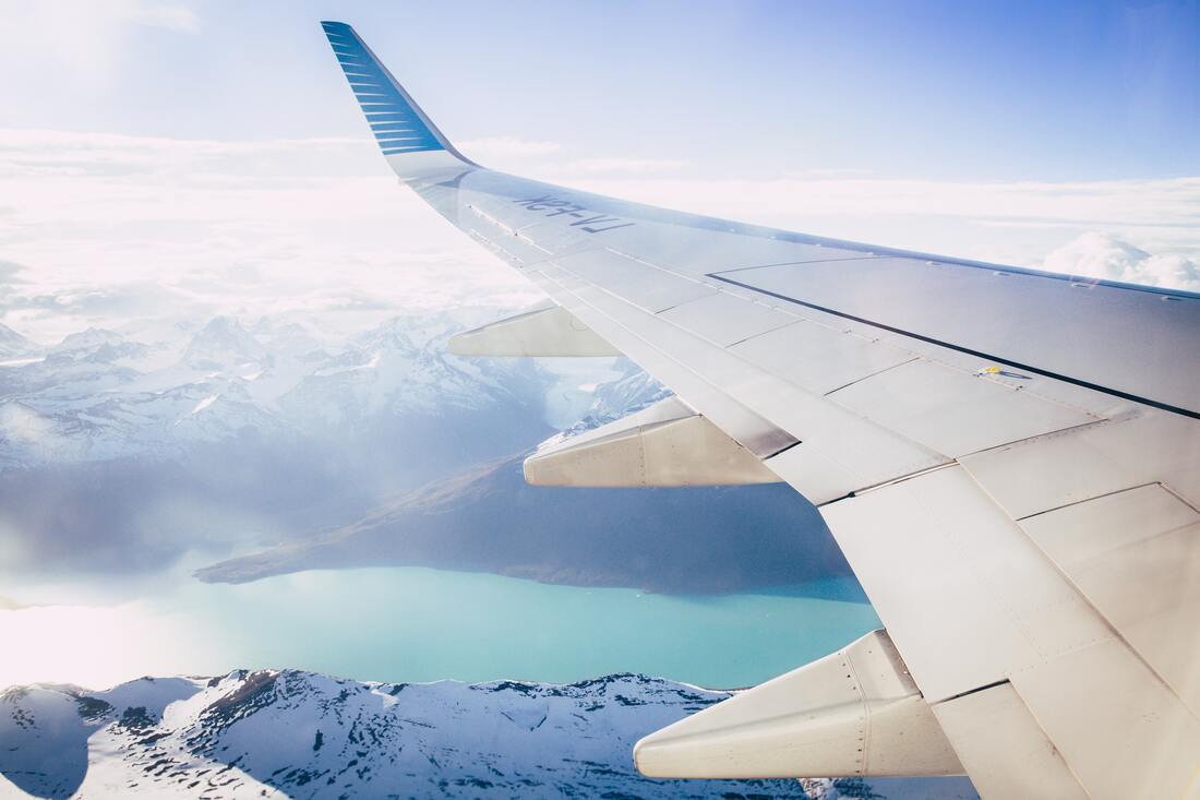 Canadian Transportation Agency Flight Delay Compensation Rules. Wing of a plane flies over a snowy mountain