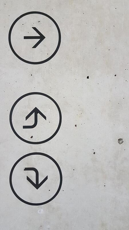 Grey concrete wall with black circles showing different directional signs.