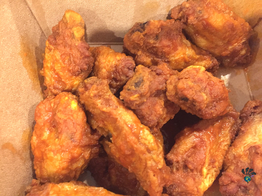 A dozen chicken wings in hot sauce sit in a cardboard takeout box