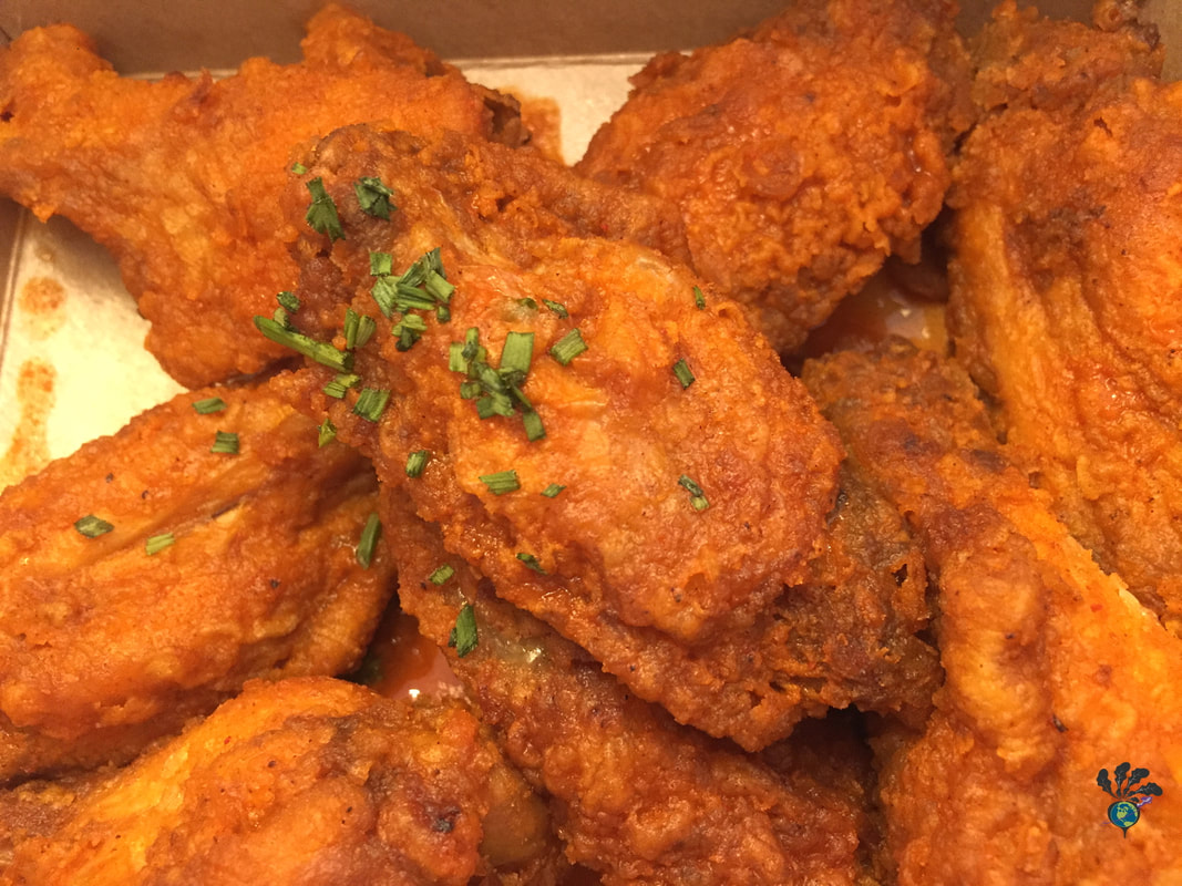 Close up of breaded wings tossed in hot sauce, with a light sprinkling of herbs on the top