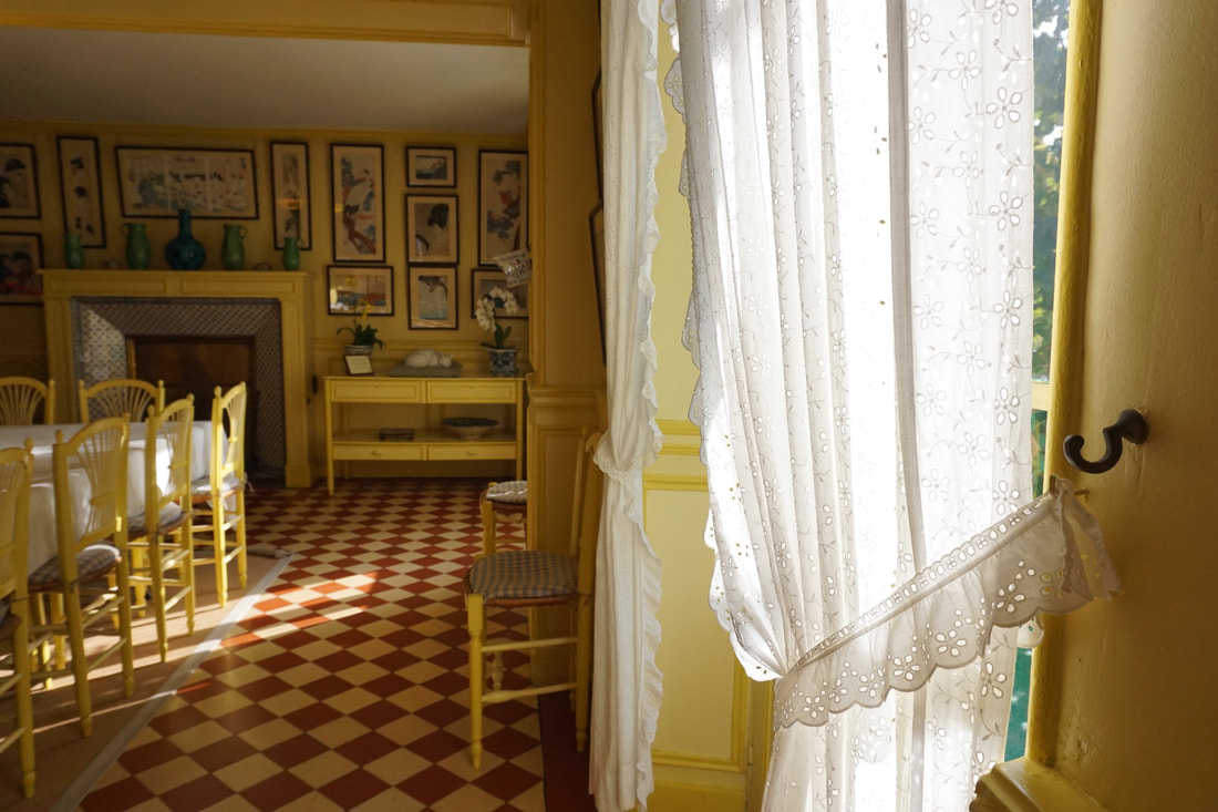 A bright yellow dining room with checkered tile floors and white lace curtains