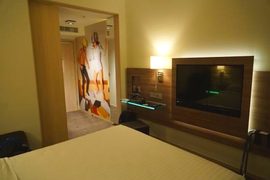 Moxy Milan Malpensa Airport Hotel Corner of bed and entrance way showing large muralsPicture