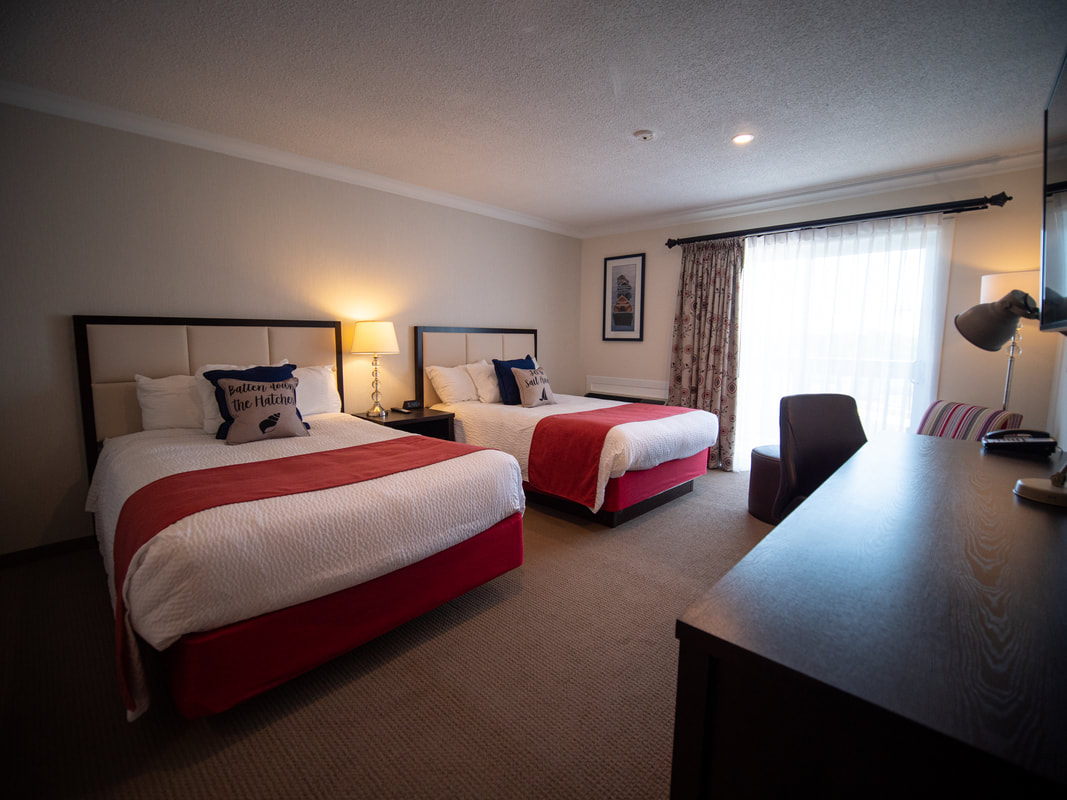 Two double beds in a hotel room with white linens and red accents. Picture
