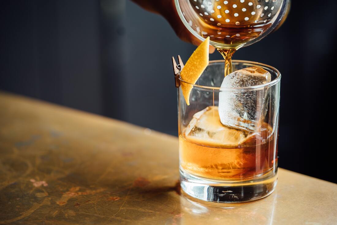 Old fashioned cocktail in a short glass with large ice and a twist of orange rind.Photo by Adam Jaime on Unsplash