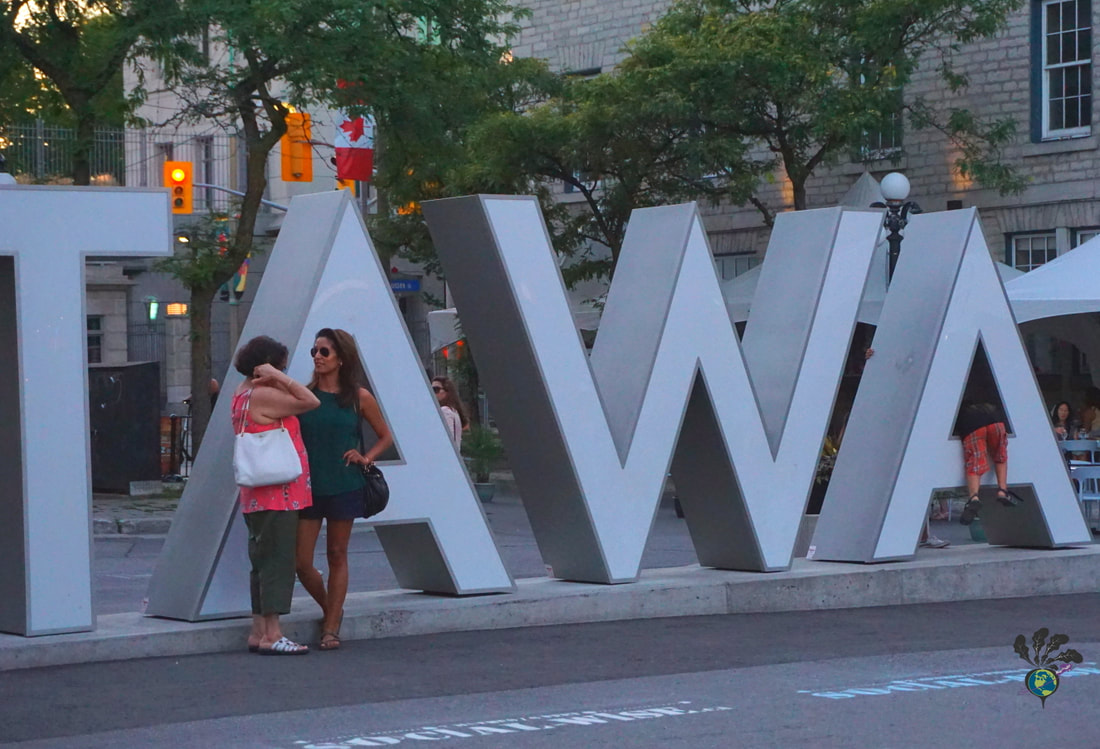 Two women chat in front of the Ottawa sign in the Byward Market