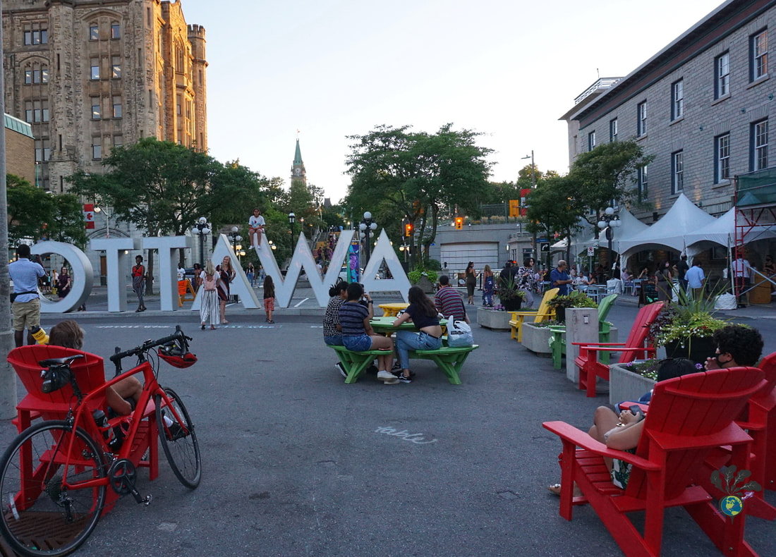 Red chairs and and tourist around the white Ottawa sign in the Byward market with the Parliament buildings in the distant background Picture