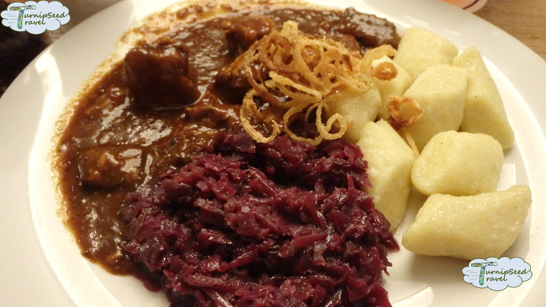 A plate of goulash, red cabbage, and potatoes